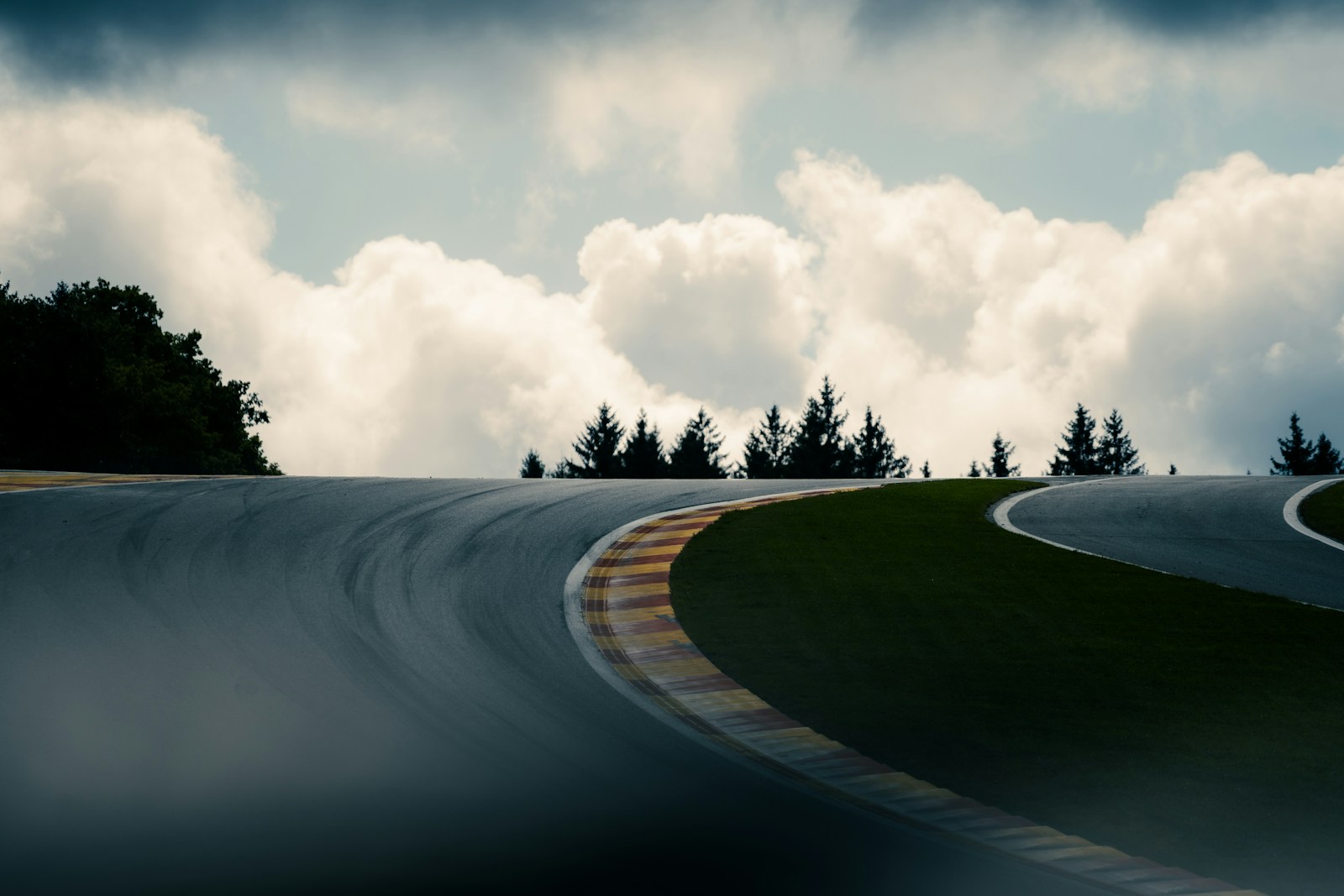 Empty asphalt race track curve under dramatic clouds — the setting for the kind of weekend Hilton × McLaren auctions unlock