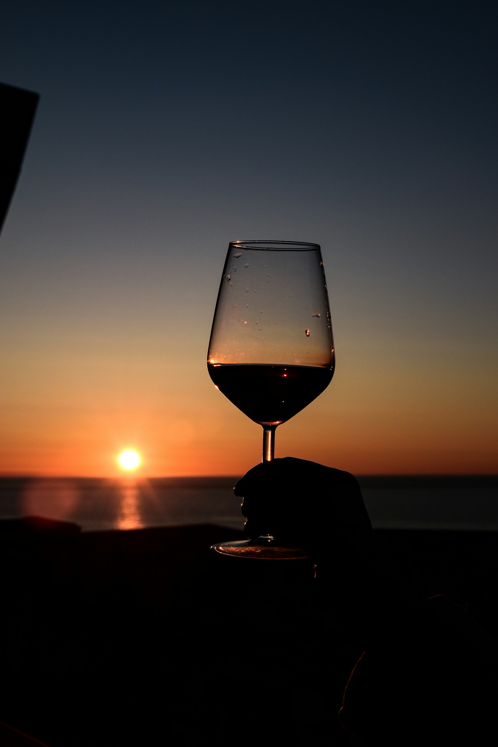 A glass of red wine silhouetted against a seaside sunset — the vibe of a Southwest Songwriters in Paradise or Pebble Beach weekend